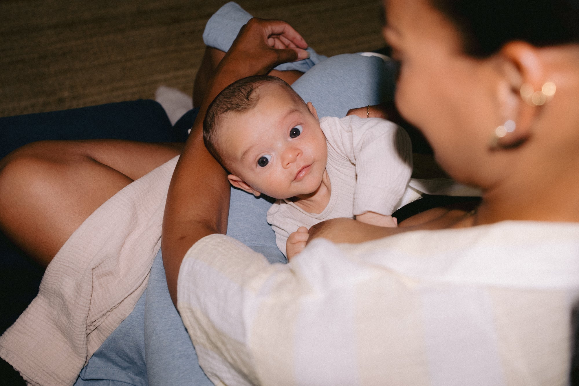 A baby gazing up at the camera while pausing during a breastfeeding session.