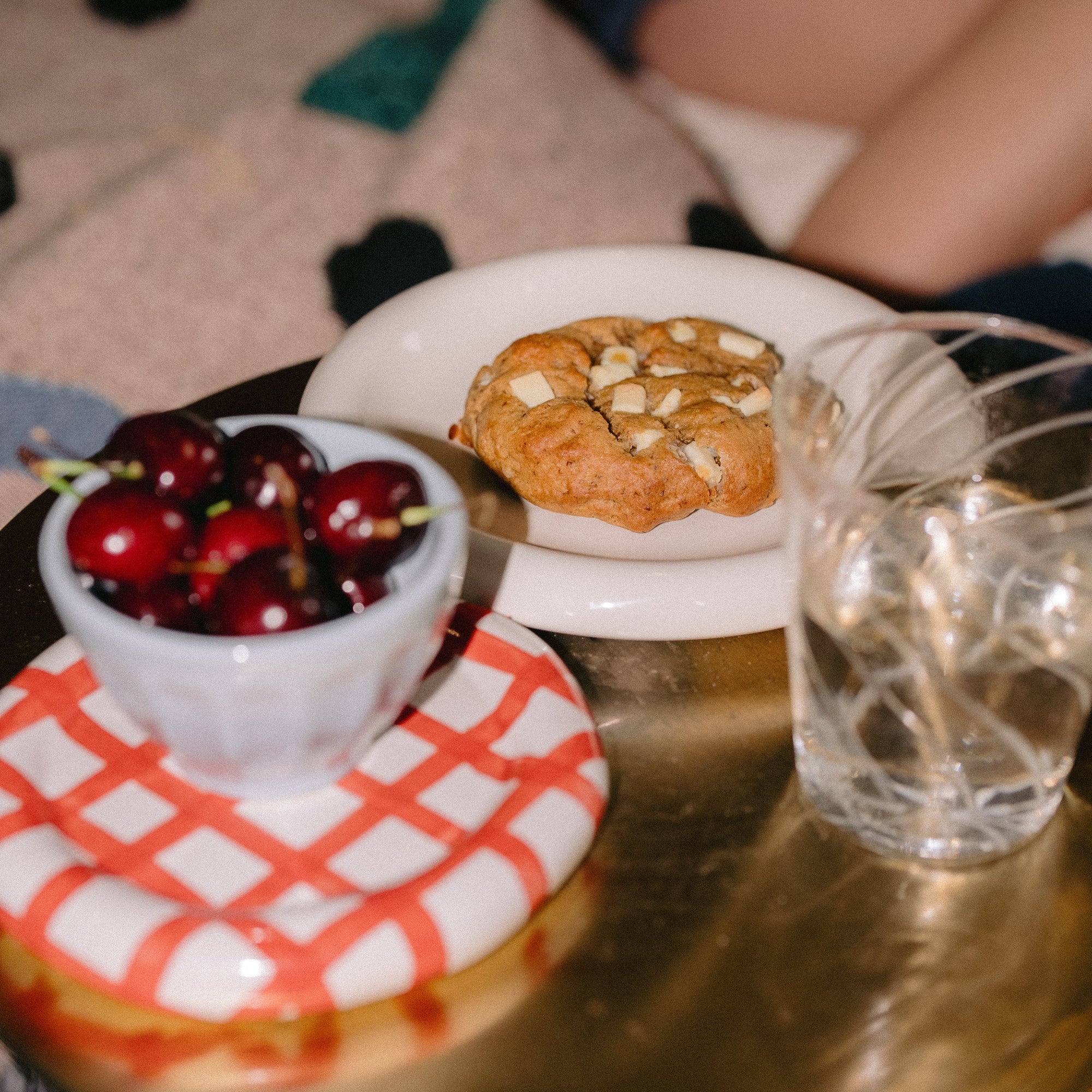 Banana pudding lactation cookie with white chocolate on a white HAY plate, styled with a glass of water and cherries in a light blue snack bowl