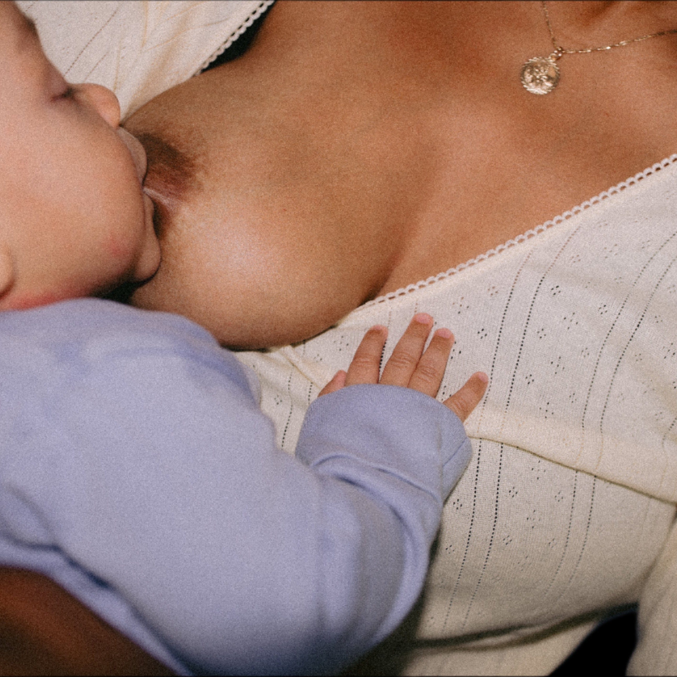 Eight-month-old baby breastfeeding in a blue onesie, resting hand on mum’s yellow pajama top