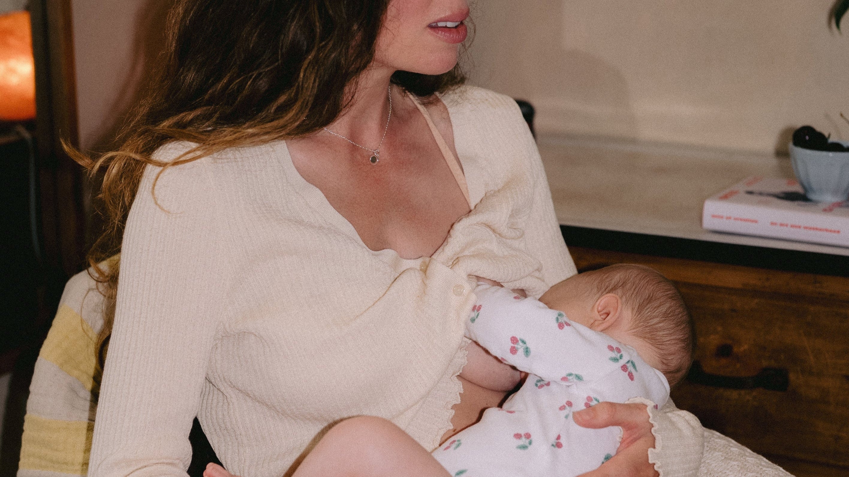 Mother breastfeeding her daughter while wearing a beige long-sleeve top, holding her close in a tender moment.
