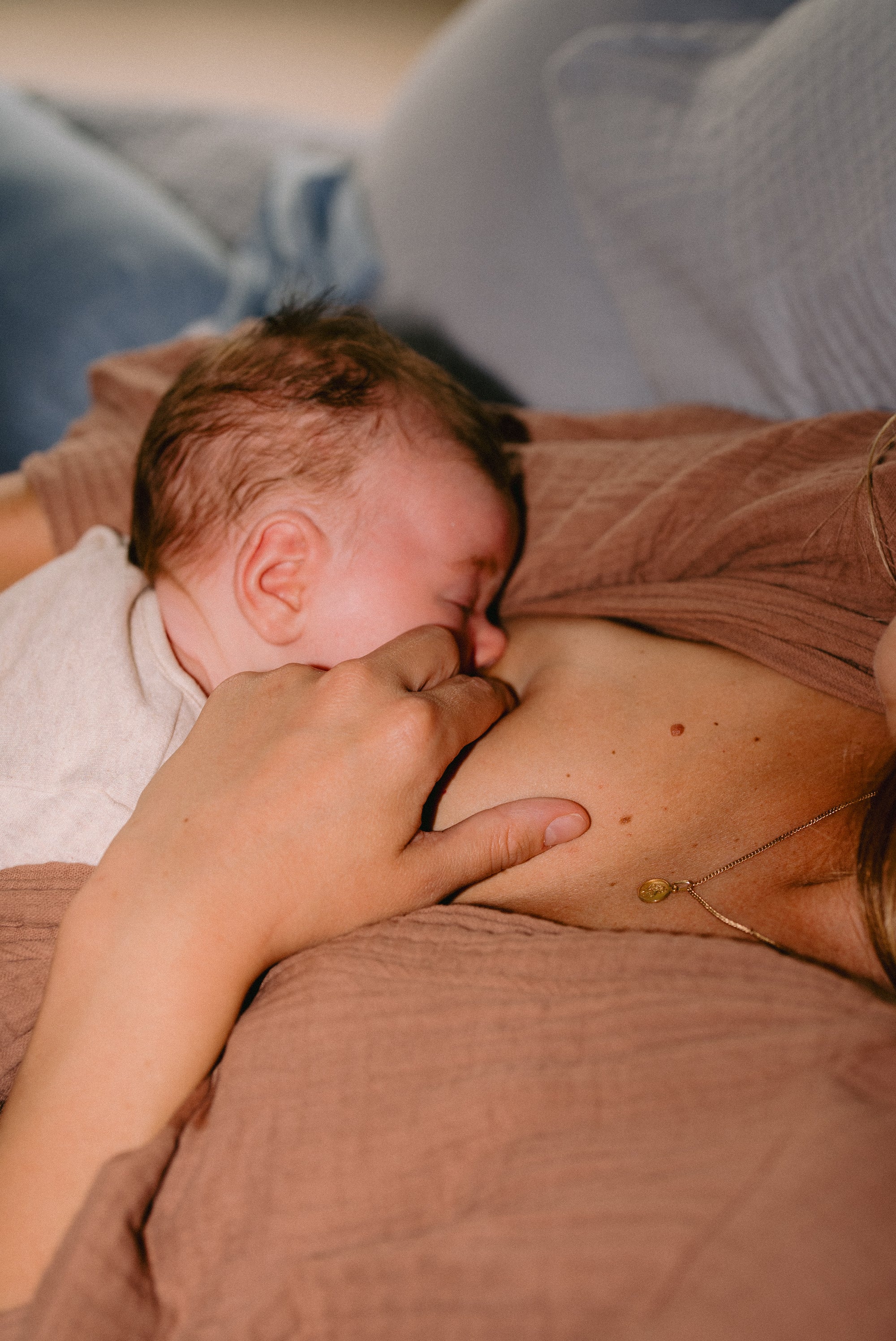 A newborn breastfeeding in a laid-back nursing position while the mother supports her breast to help with latching