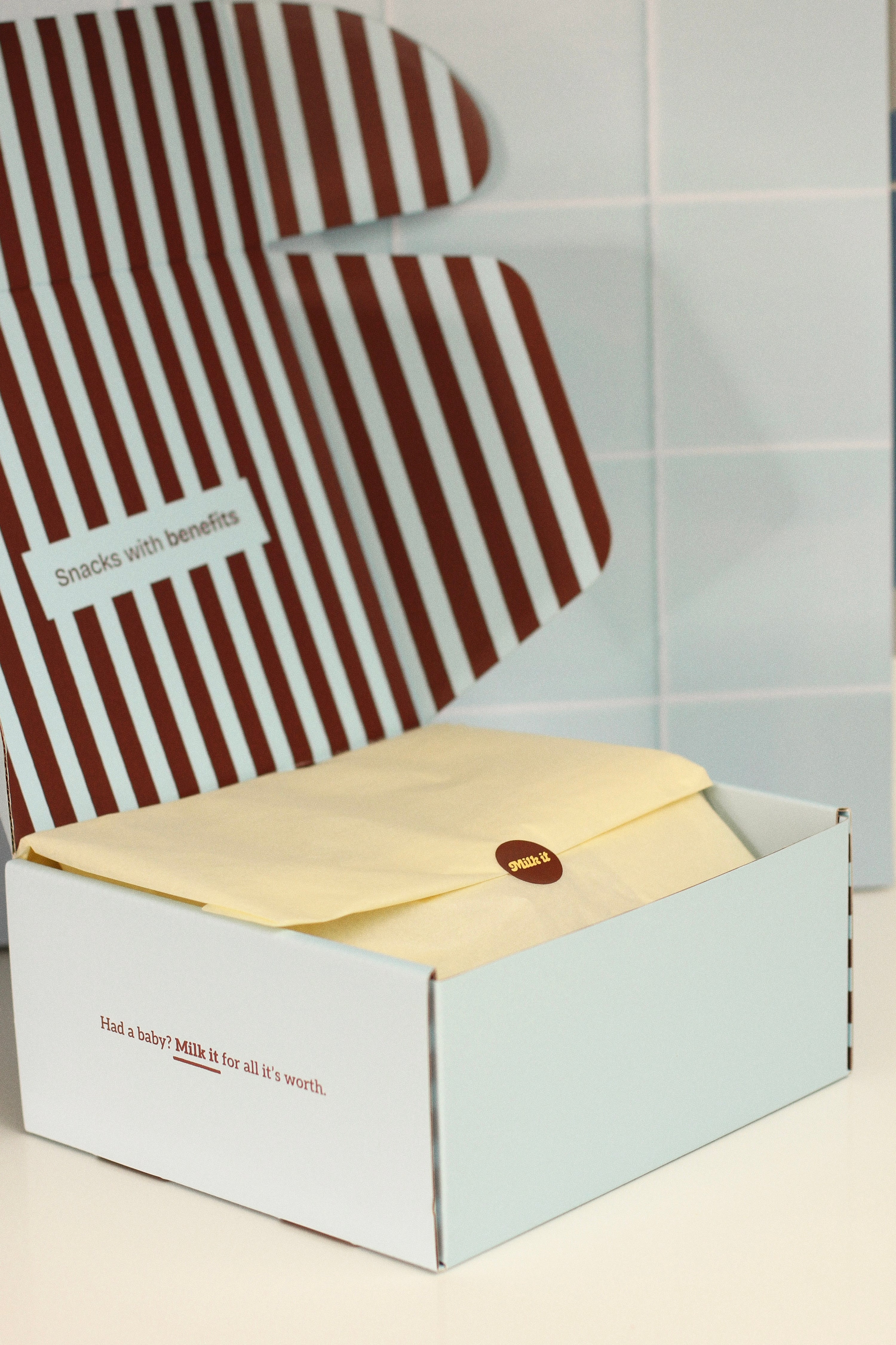 close up of a Milk it cookie box carefully wrapped in a butter yellow tissue with the words "Had a baby? Milk it for all it's worth" on the side. 