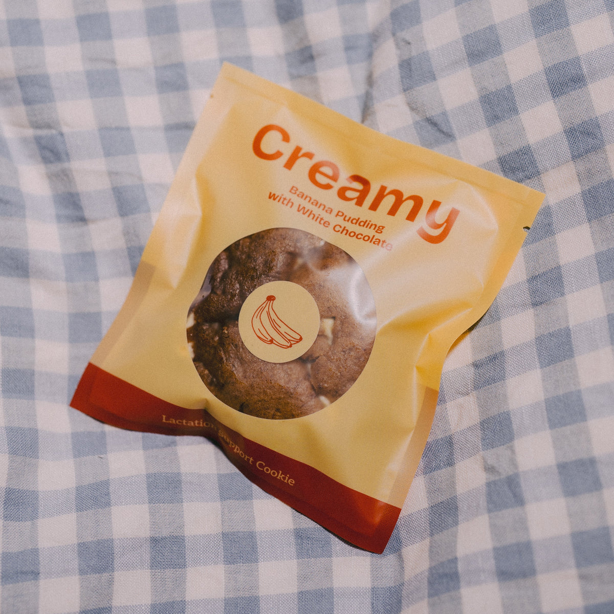 A bag of Creamy Banana Pudding  with White Chocolate lactation support Cookies, resting on a blue and white checkered blanket.