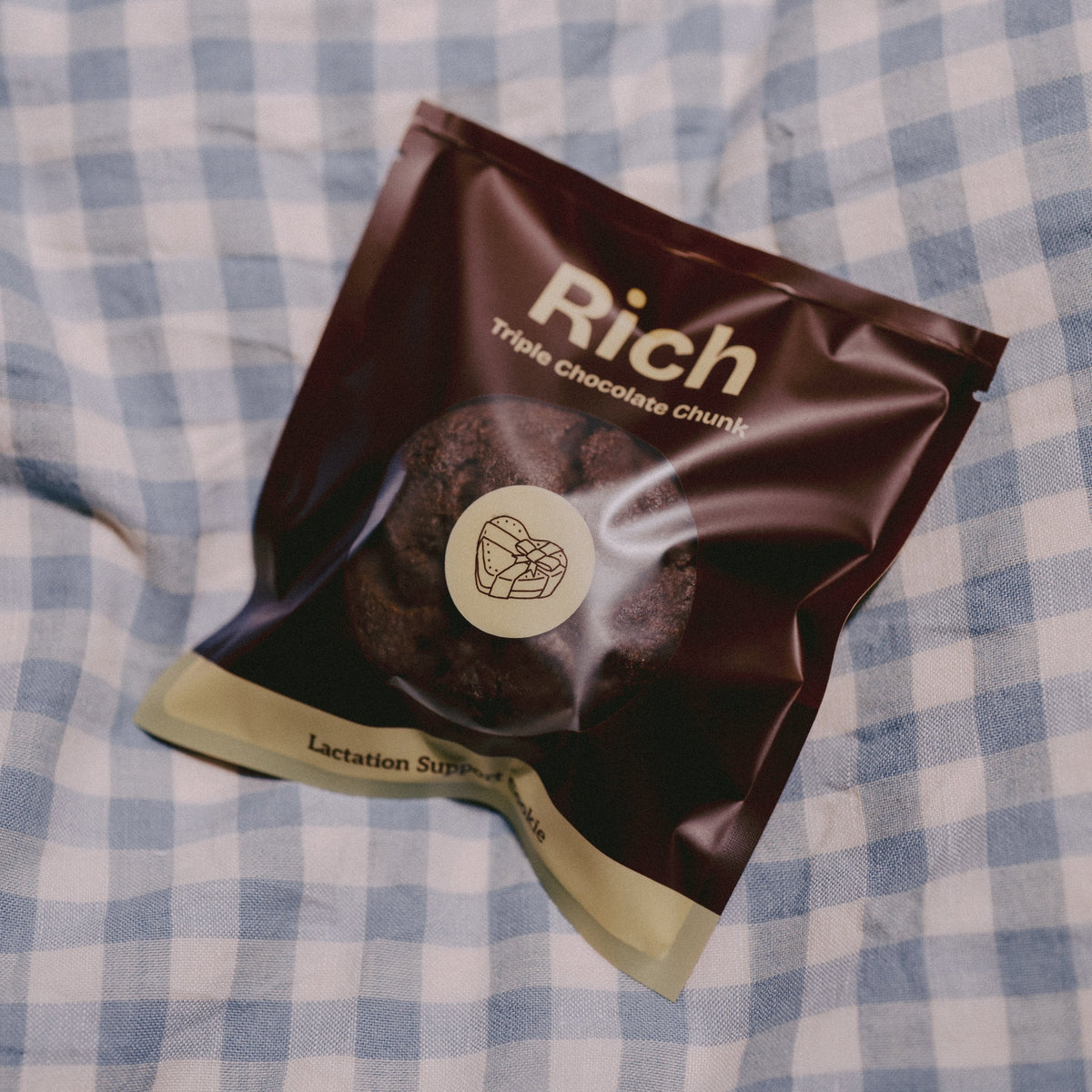A bag of Rich Triple Chocolate Chunk lactation support cookies placed on a blue and white checkered fabric surface.