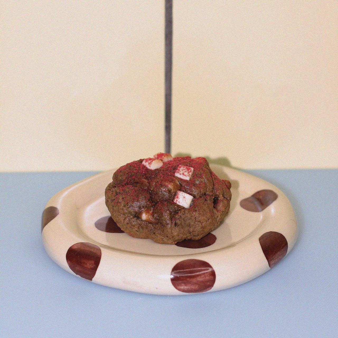 lactation cookie with organic raspberry powder and white chocolate against a butter yellow tiled wall.