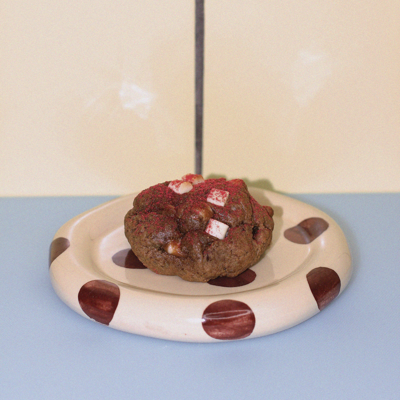 lactation cookie with organic raspberry powder and white chocolate against a butter yellow tiled wall.
