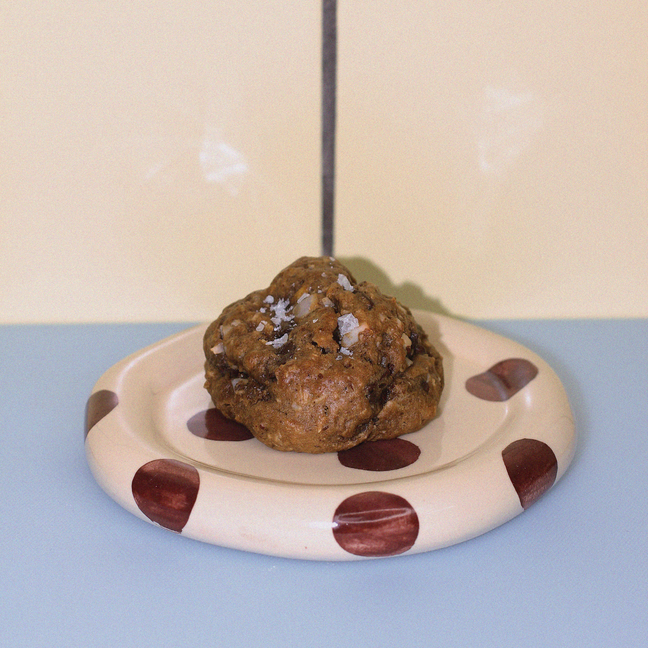 lactation cookie with  dark chocolate, pecan, cornflake, coconut and sea salt flakes against a butter yellow tiled wall