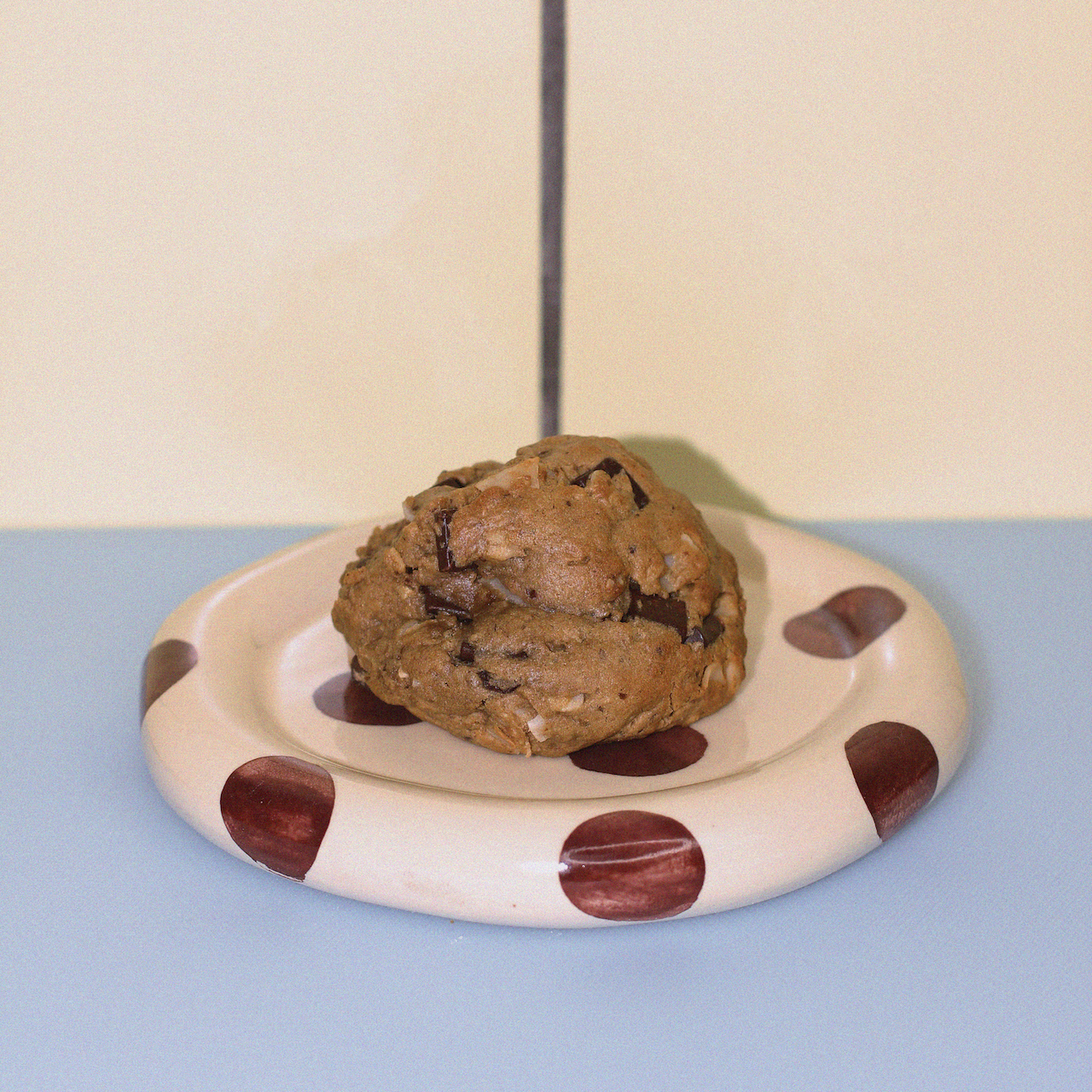 dairy-free lactation cookie with dark chocolate and coconut against a butter yellow tiled wall.
