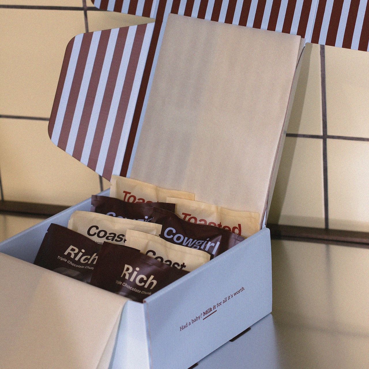 Box of assorted lactation cookies with a striped lid on a tiled surface