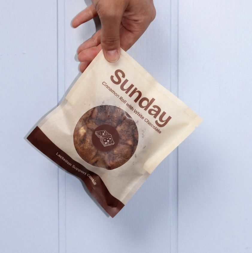 Hand holding a gluten-free cookie bag 'Sunday' against a light blue background