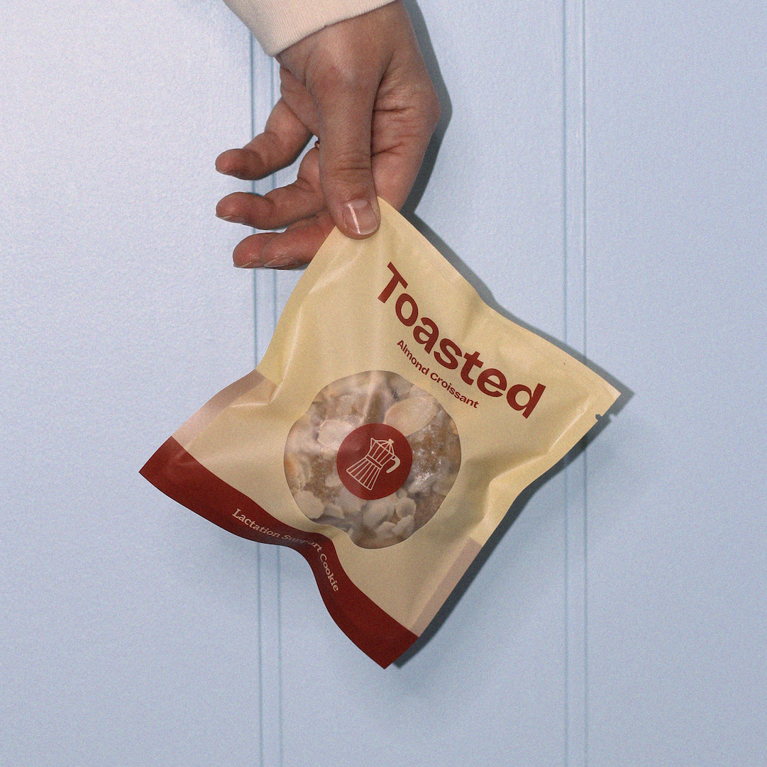 Hand holding a cookie bag 'Toasted' against a light blue background
