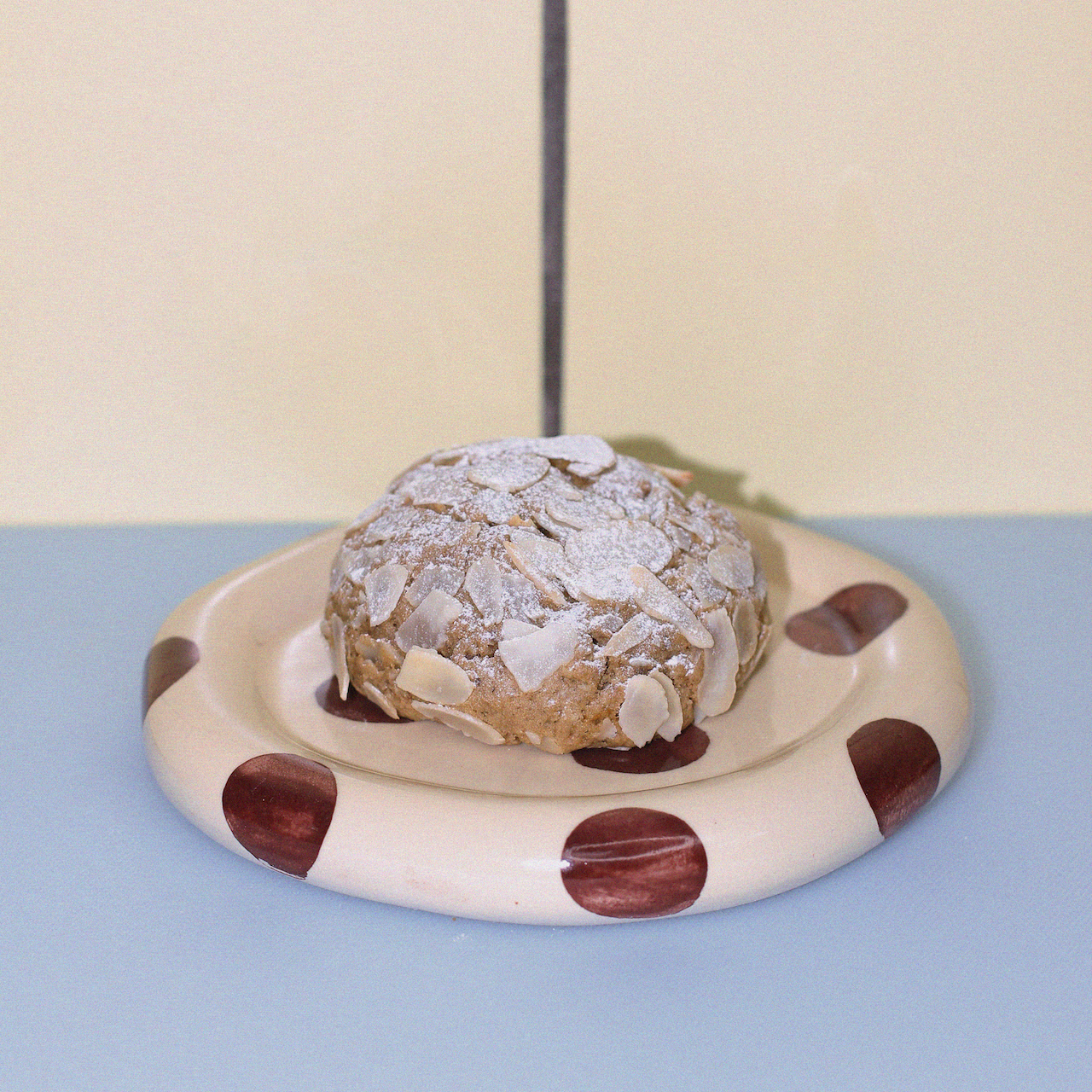 dairy free lactation cookie with toasted flaked almonds against a butter yellow tiled wall.
