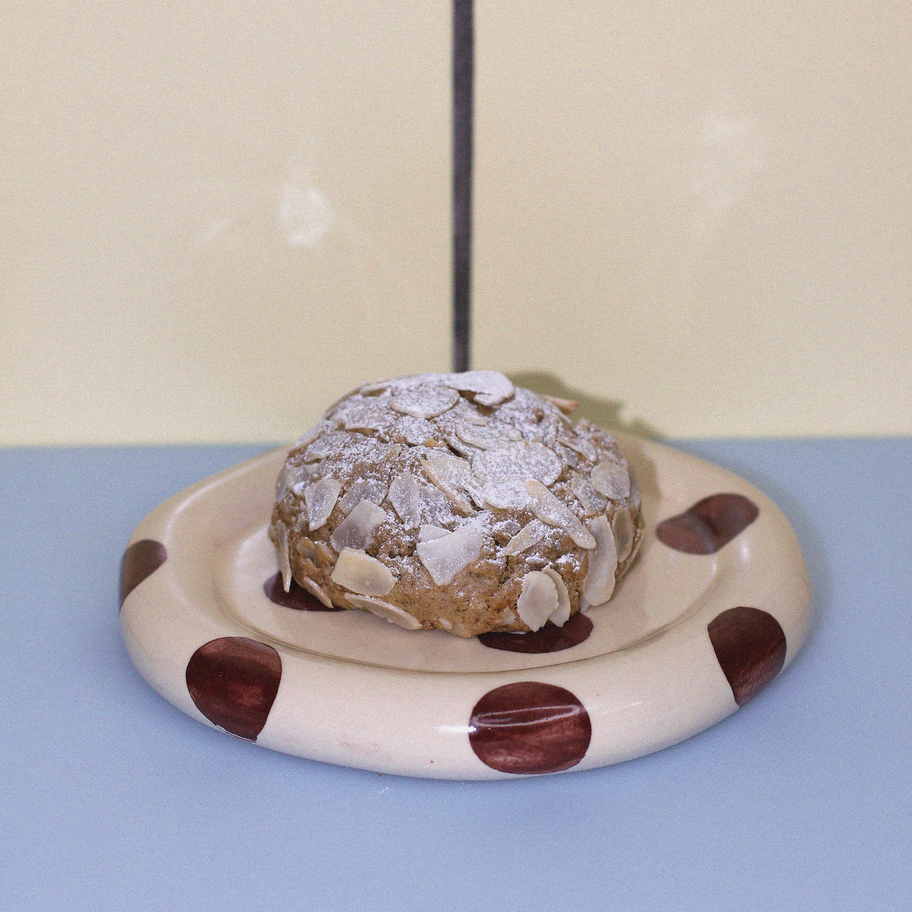 dairy free lactation cookie with toasted flaked almonds against a butter yellow tiled wall.