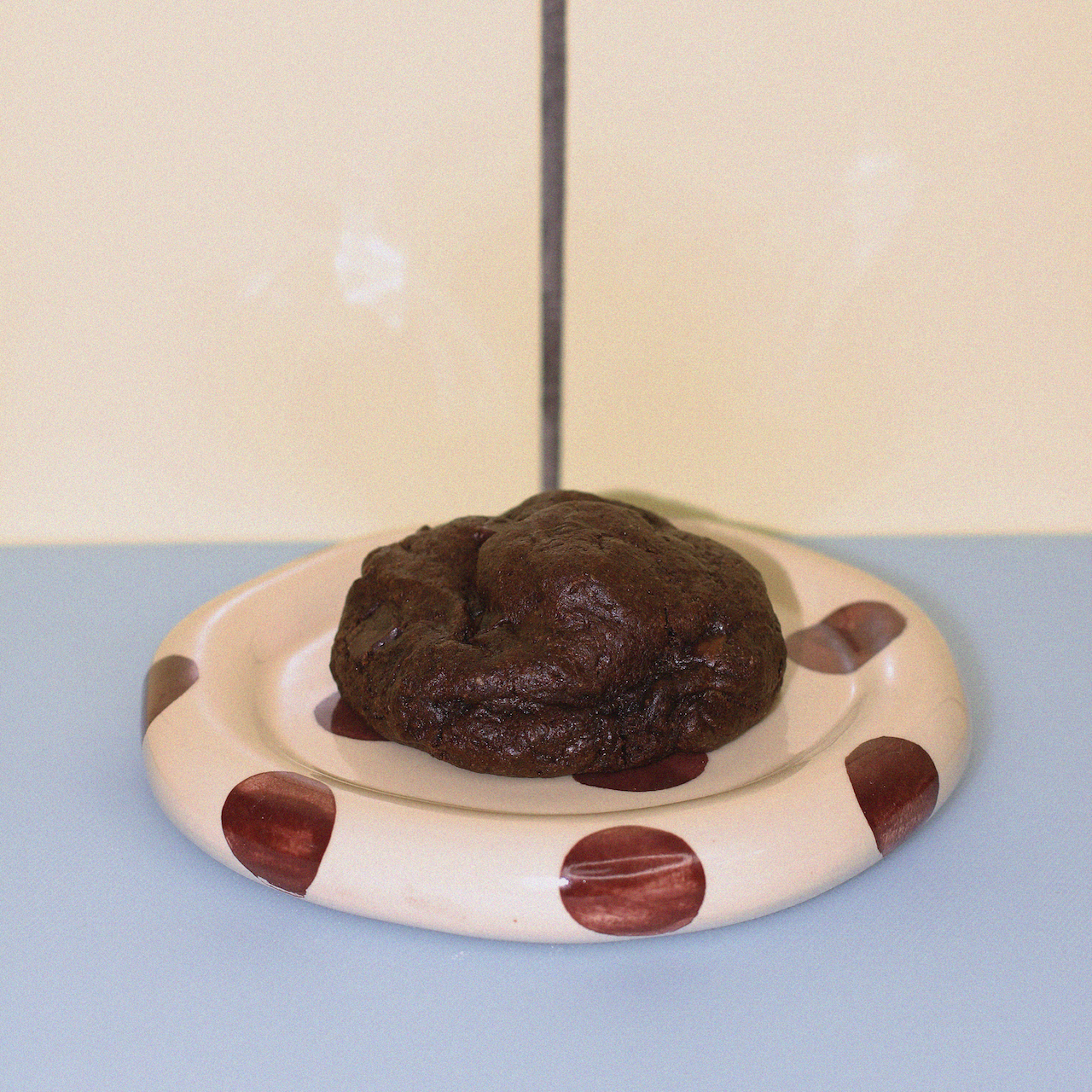 triple chocolate chunk lactation cookie against a butter yellow tiled wall