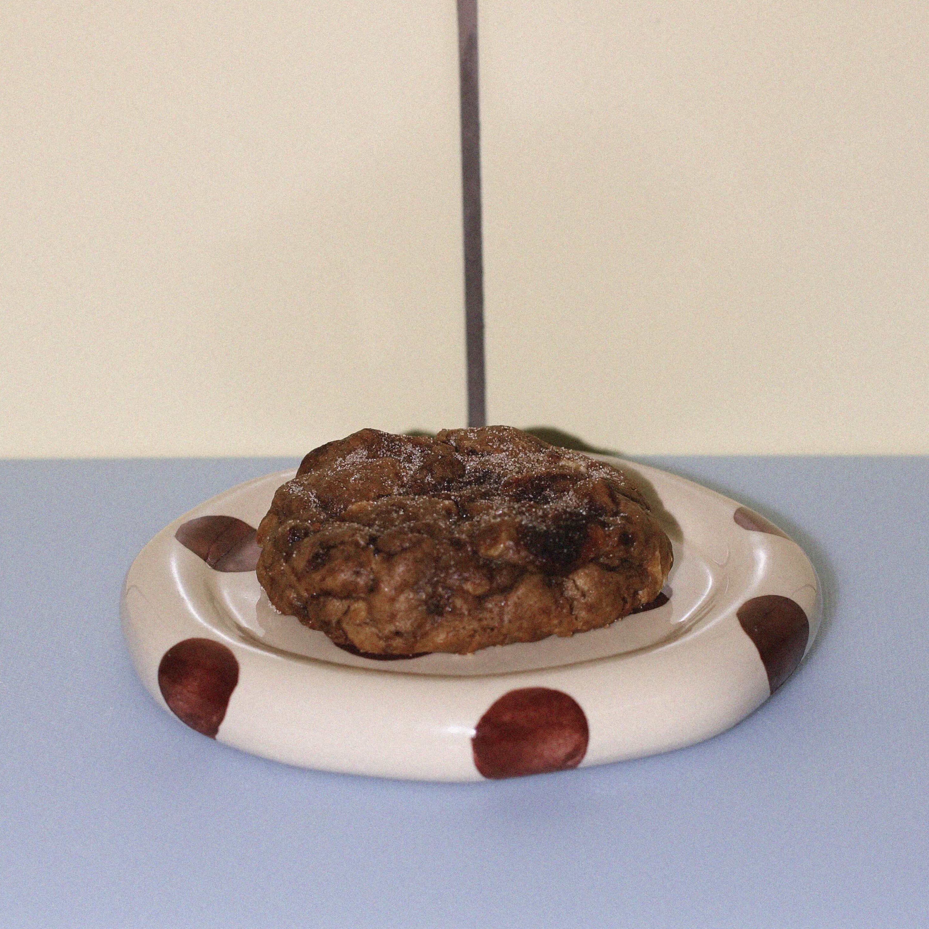 cinnamon roll with white chocolate lactation cookie against a butter yellow tiled wall